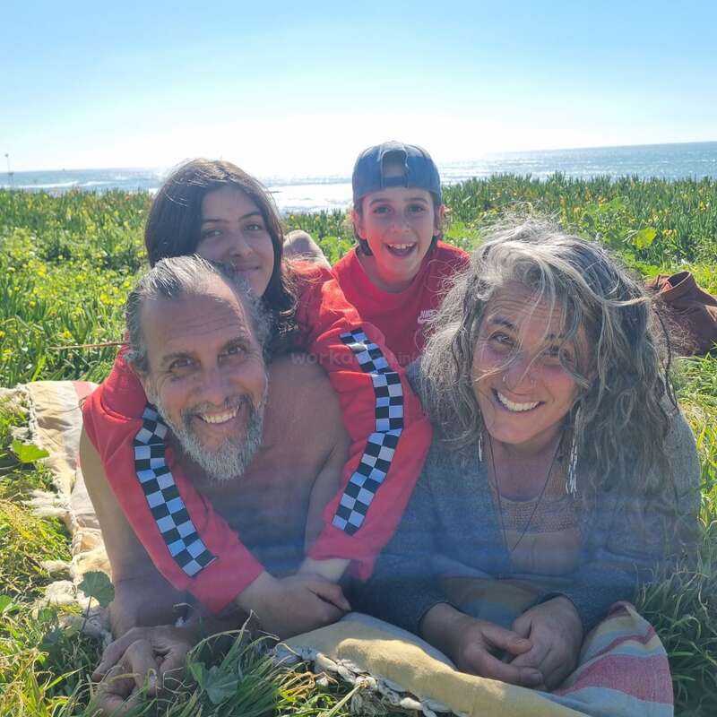 Eine glückliche vierköpfige Familie liegt lächelnd gemeinsam auf einer Decke im Gras am Meer und genießt mit Liebe und Freude einen sonnigen, wunderschönen Tag im Freien.