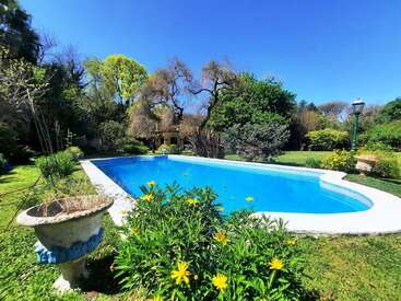 Une journée ensoleillée met en valeur une piscine d'un bleu limpide, entourée d'arbres verdoyants, de fleurs jaunes et d'un jardin paisible et bien entretenu.
