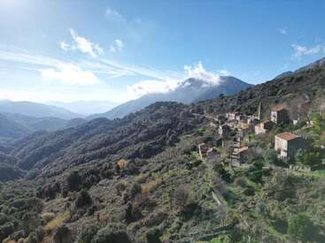 A picturesque mountain village nestles on a lush green hillside, with red-roofed houses, winding paths, and dramatic peaks under a bright blue sky. Peaceful atmosphere.