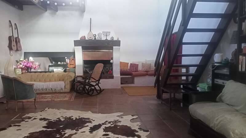 Esta sala de estar aconchegante tem lareira, cadeira de balanço, sofás, violões na parede, tapete de couro, estante, escadas e itens decorativos, criando uma atmosfera acolhedora.