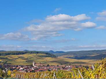 Un village pittoresque niché au milieu de collines verdoyantes et de vignobles, sous un ciel bleu éclatant parsemé de nuages blancs cotonneux. Un paysage paisible et pittoresque.