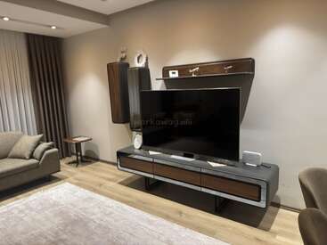 Esta sala de estar moderna apresenta uma TV grande em um console elegante, decoração minimalista, cores neutras, um sofá confortável, cortinas, um tapete e piso de madeira.