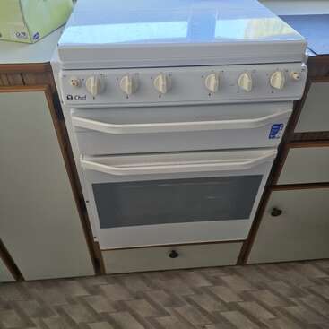 En esta imagen se ve un horno blanco de la marca Chef con cinco mandos, empotrado en una cocina entre dos armarios. El horno tiene dos tiradores horizontales y una ventana de cristal.
