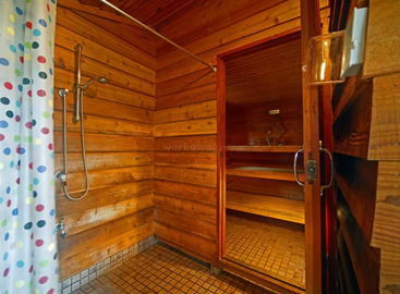 Esta imagen muestra una acogedora sauna de madera con una zona de ducha contigua. Cuenta con una cortina de ducha de lunares, suelo de baldosas y un ambiente cálido y acogedor.