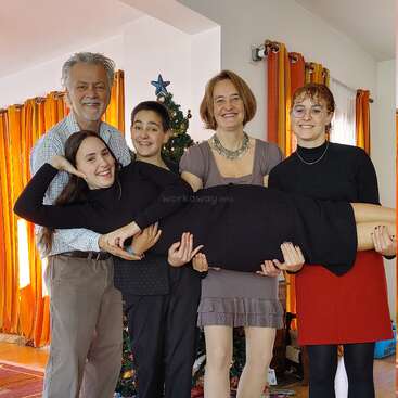 L'image représente une famille de cinq personnes posant pour une photo devant un arbre de Noël, le père tenant deux enfants et la mère en tenant un, tous souriants.