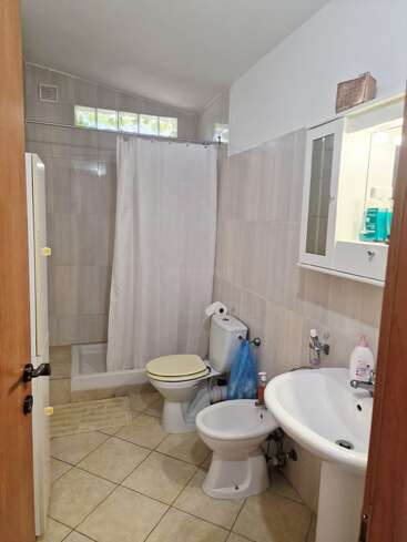 Este cuarto de baño cuenta con una ducha a ras de suelo con cortina, inodoro, bidé, lavabo, armario con espejo, paredes y suelo alicatados, y diversos artículos de aseo para el uso diario.