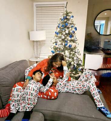 A woman and two children in matching pajamas relax on a couch by a decorated Christmas tree, enjoying a festive and cozy holiday moment together at home.