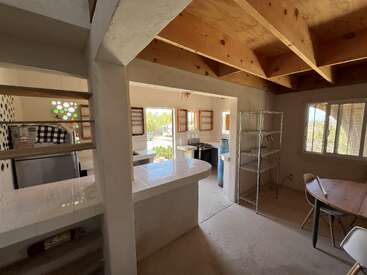 Cette image montre une cuisine rustique avec des comptoirs en carrelage blanc, des étagères ouvertes en bois, des étagères en métal, un plafond en bois apparent, de grandes fenêtres et une lumière naturelle qui éclaire l'espace.