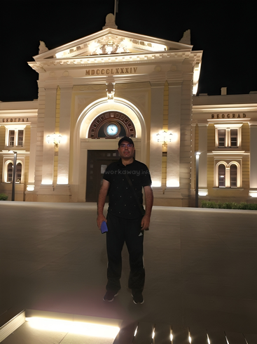Ein Mann steht vor einem beleuchteten historischen Gebäude bei Nacht. Das Gebäude mit seinen großen gewölbten Türen, römischen Ziffern, Säulen und dekorativen Lichtern bietet ein eindrucksvolles Bild.