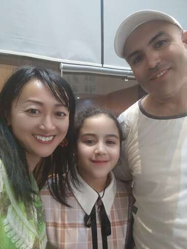 Drei Personen lächeln sich auf einem Selfie in Nahaufnahme zu. Zu der Gruppe gehören eine Frau, ein Mann mit einer weißen Mütze und ein junges Mädchen. Gemütliche Atmosphäre.