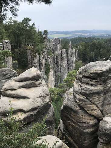 Formações rochosas gigantescas erguem-se de forma espetacular de uma floresta verdejante. Altas torres de pedra e rochas arredondadas dominam a paisagem sob um céu nublado. Uma natureza impressionante.