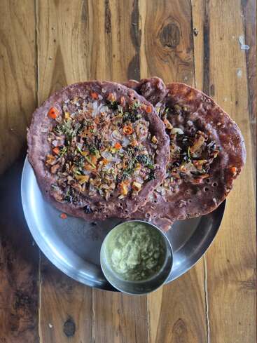 Cette image montre deux dosas ragi nutritifs garnis de légumes hachés, servis sur une assiette en acier inoxydable. Ils sont accompagnés d'un chutney à la noix de coco.
