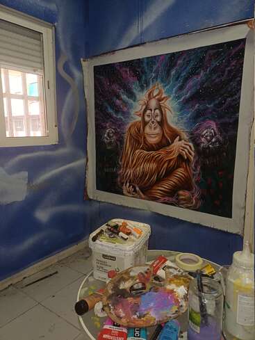 En una pared azul cuelga un vibrante y colorido cuadro de un orangután. En la pequeña mesa redonda que hay debajo, hay material artístico, como una paleta y pinceles.