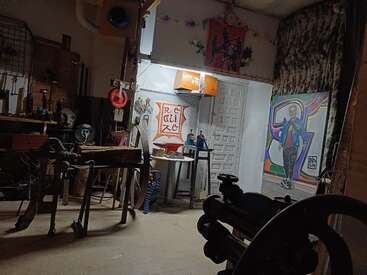 Un estudio de arte ecléctico y tenuemente iluminado con herramientas, mesas de trabajo, cuadros, un colorido retrato, adornos dispersos y un cartel de "REALIZE", que crean un ambiente creativo y ligeramente desordenado.