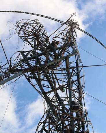 Esta imagen muestra una gran escultura de alambre de un arquero, hecha de metal, con gente trepando por ella contra un cielo azul salpicado de nubes. Impresionante instalación artística.