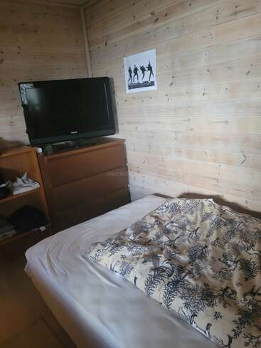 Esta acogedora habitación con paredes de madera cuenta con una cama con un edredón estampado, una cómoda con un televisor encima, estantes abiertos y un póster con una silueta bailando.