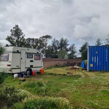 The image shows a small, open area with a few trees and a body of water in the background. The area is surrounded by a fence and has a few buildings and structures.