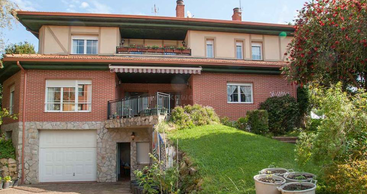 Cette image montre une maison en briques de deux étages dotée d'un toit végétalisé, de grandes fenêtres, d'un garage, d'un balcon, d'un jardin en pente et d'une végétation luxuriante.