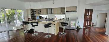 Diese moderne Küche verfügt über eine Insel mit vier Barhockern, Edelstahlgeräte, Holzböden, große Fenster und Glasschiebetüren mit Blick auf einen üppigen Innenhof.