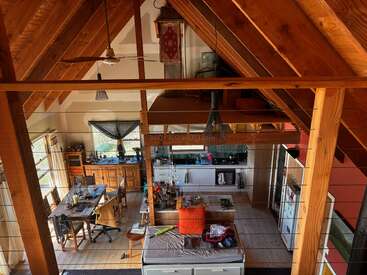 Esta imagem mostra um loft aconchegante, de madeira, em plano aberto, com vigas expostas, cozinha, sala de jantar, sala de estar e um espaço para dormir no mezanino superior.