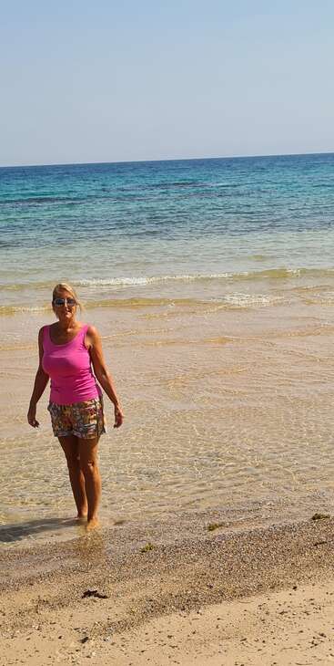 The image depicts a woman strolling along a sandy beach, with the ocean\'s waves gently lapping at the shore behind her, creating a serene atmosphere.