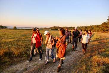 Eine Gruppe von Menschen geht bei Sonnenuntergang einen Feldweg entlang und genießt die Natur und die Gesellschaft der anderen unter einem klaren Himmel.