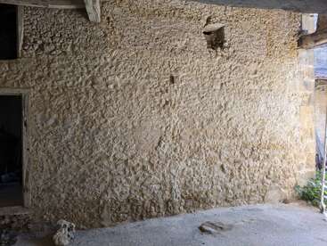 A rough, textured stone wall with an irregular surface is shown. There are small openings and a doorway, suggesting an old, rustic building structure.