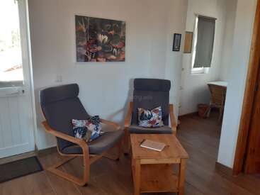Ce coin salon confortable comprend deux fauteuils gris modernes avec des coussins aux couleurs vives, une table en bois avec un ordinateur portable, des décorations murales et un petit espace de travail adjacent.