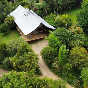 L'image représente un cadre tropical serein, avec une grande maison dotée d'un vaste jardin, entourée d'une végétation luxuriante et d'une étendue d'eau tranquille, évoquant un sentiment de paix et de détente.
