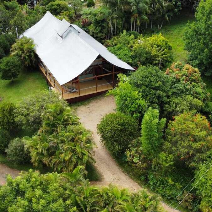 La imagen representa un entorno tropical sereno, con una gran casa con un extenso jardín, rodeada de exuberante vegetación y una tranquila masa de agua, que evoca una sensación de paz y relajación.