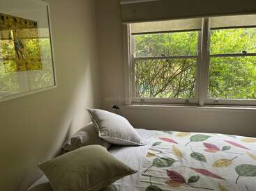 Das Bild zeigt ein ruhiges Schlafzimmer mit einem Bett, Kissen und einem Fenster, das den Blick auf das üppige Grün draußen freigibt. Der Raum ist gut beleuchtet und einladend.