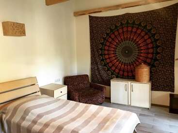 Esse quarto tem uma cama de solteiro com um cobertor listrado, uma poltrona estampada, móveis brancos e uma tapeçaria mandala colorida pendurada na parede.