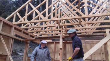 Das Bild zeigt eine Baustelle mit einem Holzgerüst und einem Stapel Holz, wahrscheinlich für ein Haus oder Gebäude, mit einem klaren und organisierten Layout. Die Szene ist gut organisiert und aufgeräumt.