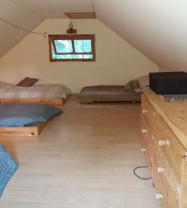 Das Bild zeigt ein Zimmer mit schrägen Decken, zwei Betten, einer Kommode und einem Fenster, das eine einfache und gemütliche Inneneinrichtung zeigt.