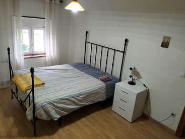 A cozy bedroom with a metal bed frame, striped bedding, a yellow blanket, white curtains, wooden floor, nightstand with a lamp, and minimalistic wall decor.