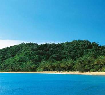 The image depicts a serene tropical beach scene, featuring a sandy shore, vibrant blue water, lush greenery, and a clear blue sky with minimal cloud cover.