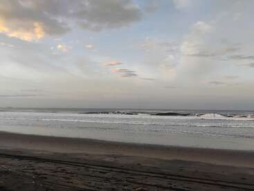 Una playa tranquila y vacía con suaves olas bajo un cielo nublado. La suave luz del sol ilumina la escena, creando un ambiente costero sereno y tranquilo.