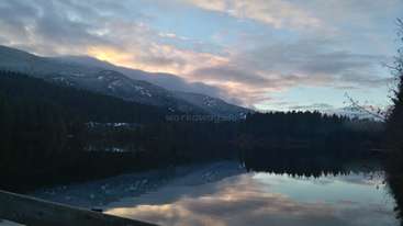 L'image représente un paysage serein avec une étendue d'eau, des arbres et une chaîne de montagnes, évoquant un sentiment de tranquillité et de beauté naturelle. Il s'agit probablement d'un lac ou d'une rivière.