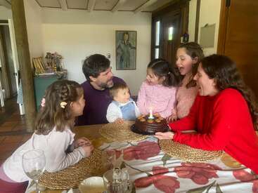 Eine Familie versammelt sich um einen Tisch, um einen Geburtstag mit einem Schokoladenkuchen und einer brennenden Kerze zu feiern. Alle lächeln herzlich und schaffen eine fröhliche, vertraute Atmosphäre.