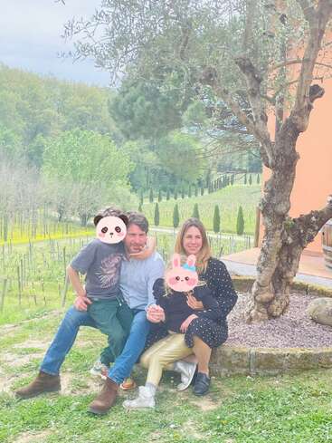 Una familia de cuatro miembros está sentada al aire libre junto a un árbol, rodeada de vegetación. Los niños tienen la cara cubierta de pegatinas con caras de animales muy monas y sonríen todos juntos.