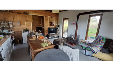 Este acogedor espacio cuenta con paredes de madera, una cocina, una estufa de leña, muebles eclécticos, una guitarra, grandes ventanales y una mesa con frutas y aperitivos.