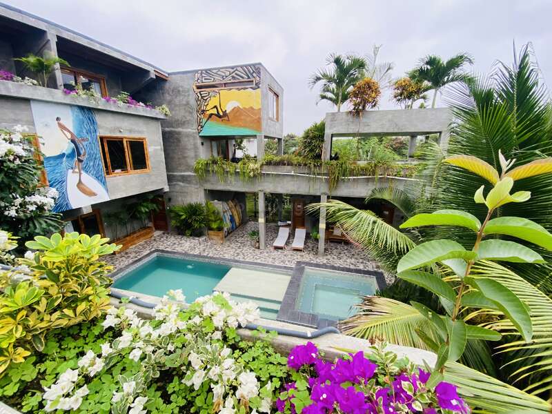 A modern villa with vibrant murals, lush tropical plants, and an inviting swimming pool. Comfortable lounge chairs and colorful flowers create a relaxing, artistic atmosphere.
