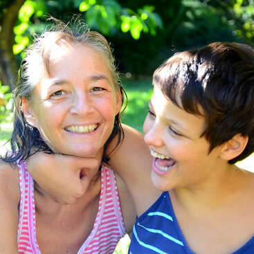 L'image représente une femme et un enfant dans une pose ludique, la main de la femme sous le menton de l'enfant et le bras de l'enfant autour de son cou.