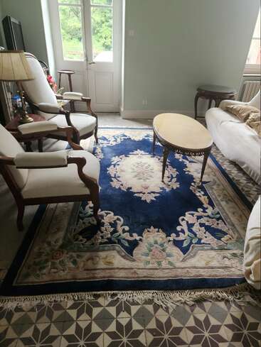 Dieses gemütliche Wohnzimmer besticht durch elegante Sessel, ein weißes Sofa, einen zierlichen ovalen Couchtisch, einen blauen Teppich mit Blumenmuster, Fliesen im Vintage-Stil und natürliches Tageslicht.