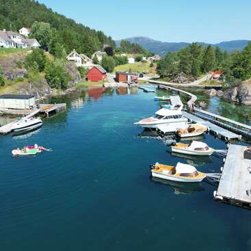 Essa pacata vila costeira apresenta águas azuis claras, vários barcos atracados, pessoas flutuando, casas de barco vermelhas, colinas arborizadas e casas charmosas aninhadas entre árvores verdes.
