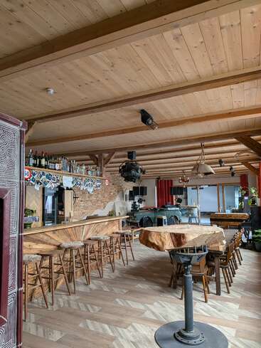 Este acogedor bar de estilo rústico cuenta con vigas de madera, una mesa de madera con bordes sin pulir única en su género, taburetes, detalles de ladrillo, lámparas colgantes y estanterías repletas de botellas, lo que crea un ambiente cálido y acogedor.
