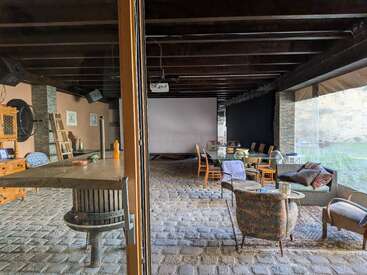 Esta acogedora habitación cuenta con suelo de adoquines, vigas de madera, una gran pantalla, varias sillas, una mesa vintage y una decoración rústica, lo que crea un ambiente relajado y acogedor.