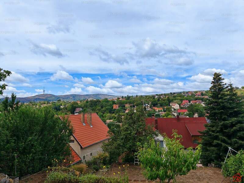 A imagem retrata uma paisagem serena com casas, árvores e montanhas sob um céu nublado, com uma pequena cidade aninhada entre as colinas à distância.