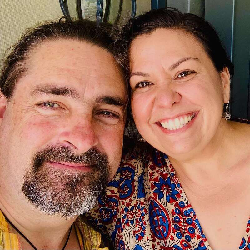 A imagem mostra um close-up de um homem e uma mulher posando para uma selfie, com a cabeça da mulher apoiada no ombro do homem.