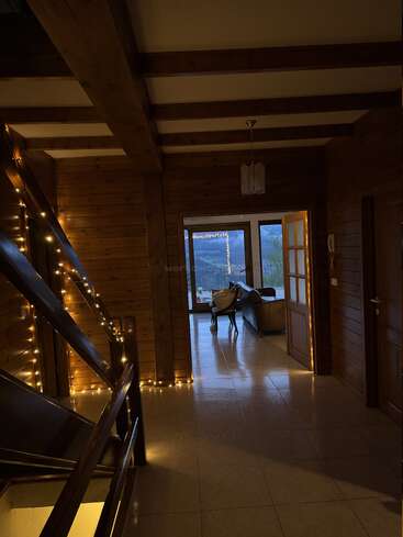 Dieser gemütliche Flur aus Holz besticht durch Lichterketten entlang der Treppe, Fliesenböden, einen Kronleuchter und ein einladendes Wohnzimmer mit großen Fenstern, die einen malerischen Blick auf die Berge bieten.